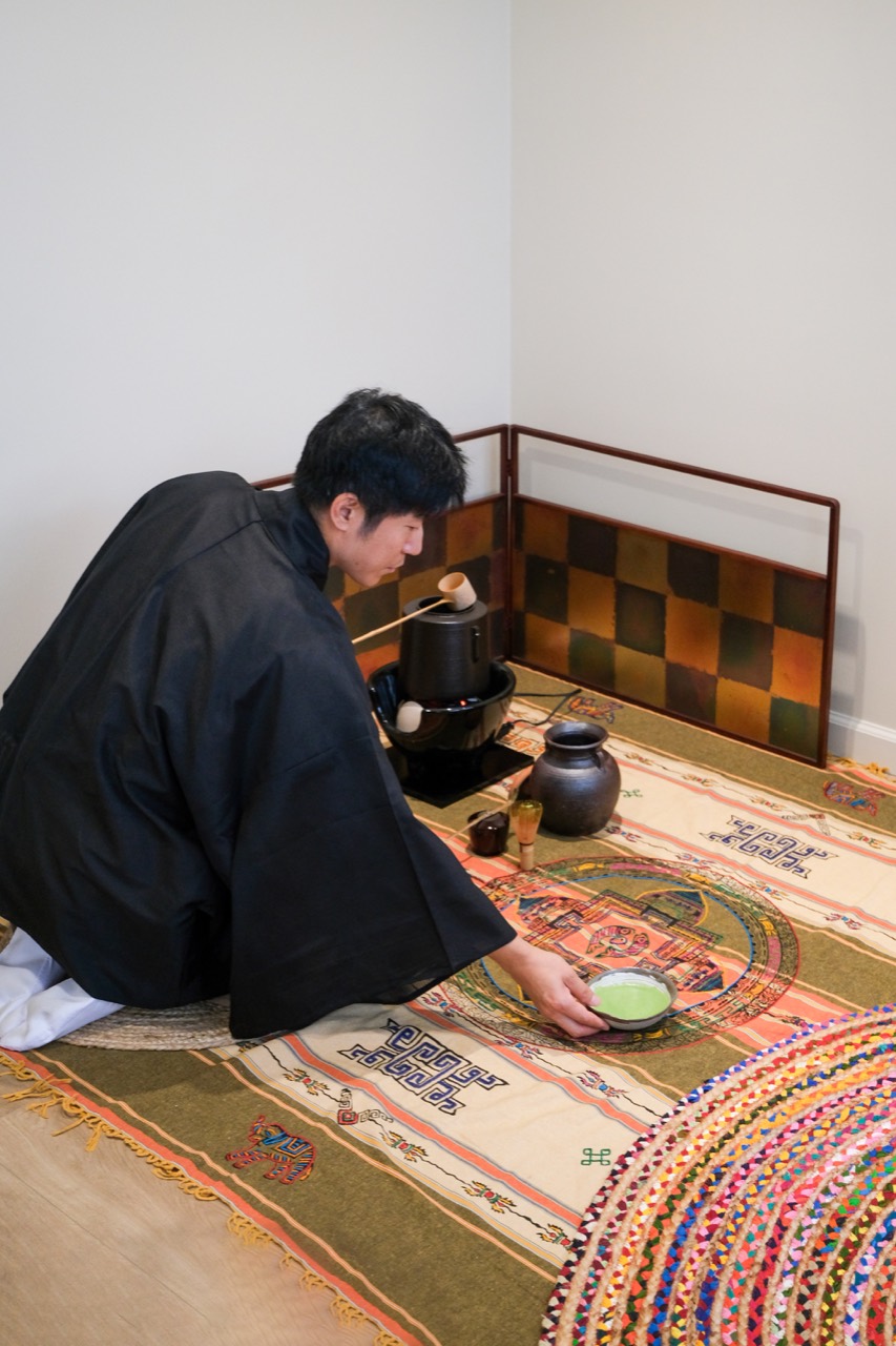Chris Yao presenting a bowl of matcha in a contemporary tea setting arranged on a patterned textile