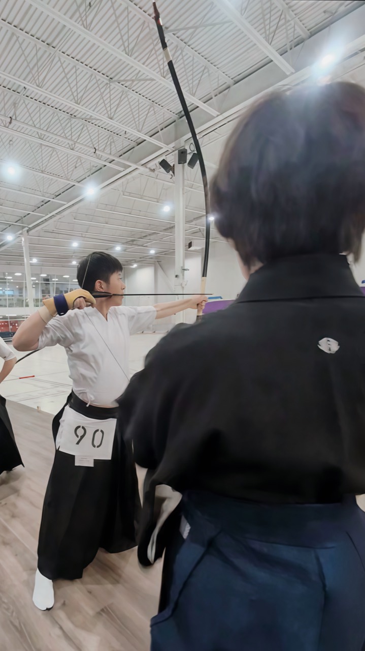 Chris Yao at full draw while a senior instructor observes closely during a kyūdō seminar in Vancouver